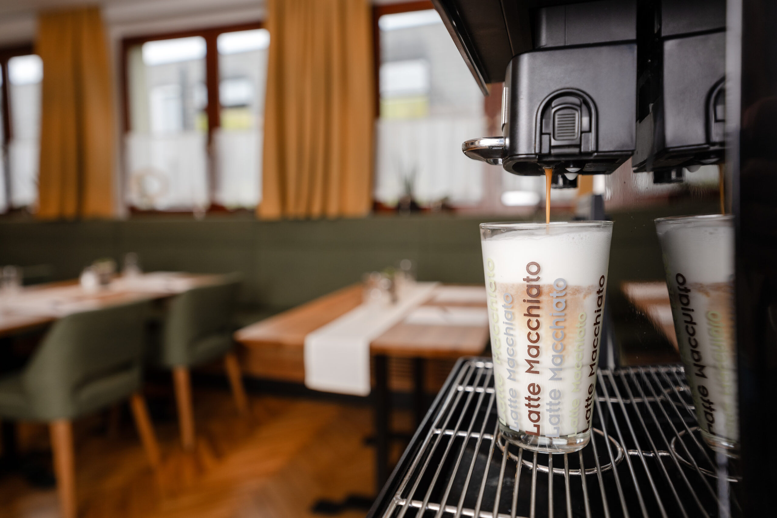Frisch zubereiteter Latte Macchiato unter einer Kaffeemaschine, fertig geschichtet mit Milchschaum und Espresso, servierbereit zum Genießen.