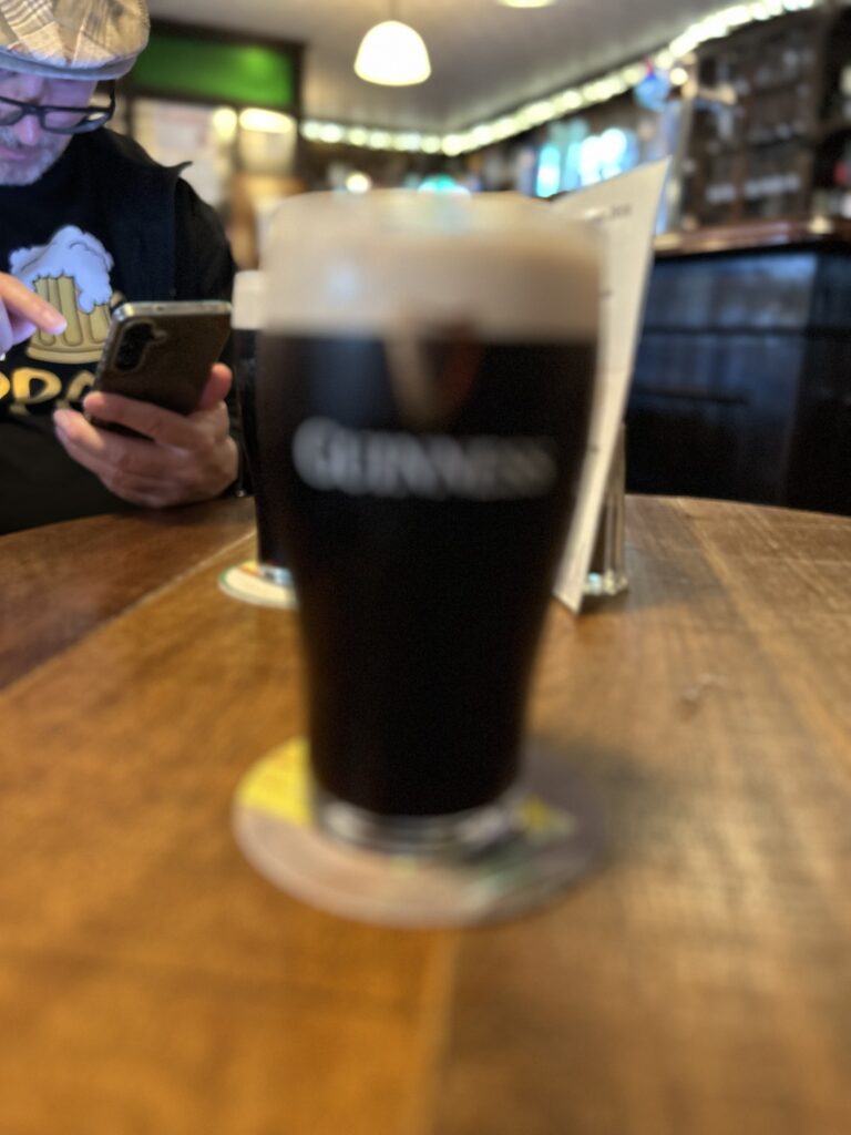 Ein Pint Bier in der Feehan's Bar in Cashel. Im Hintergrund sitzt Kurt vom Pfänderbräu und beschäftigt sich vermutlich mit dem nächsten Untappd-Check-in.