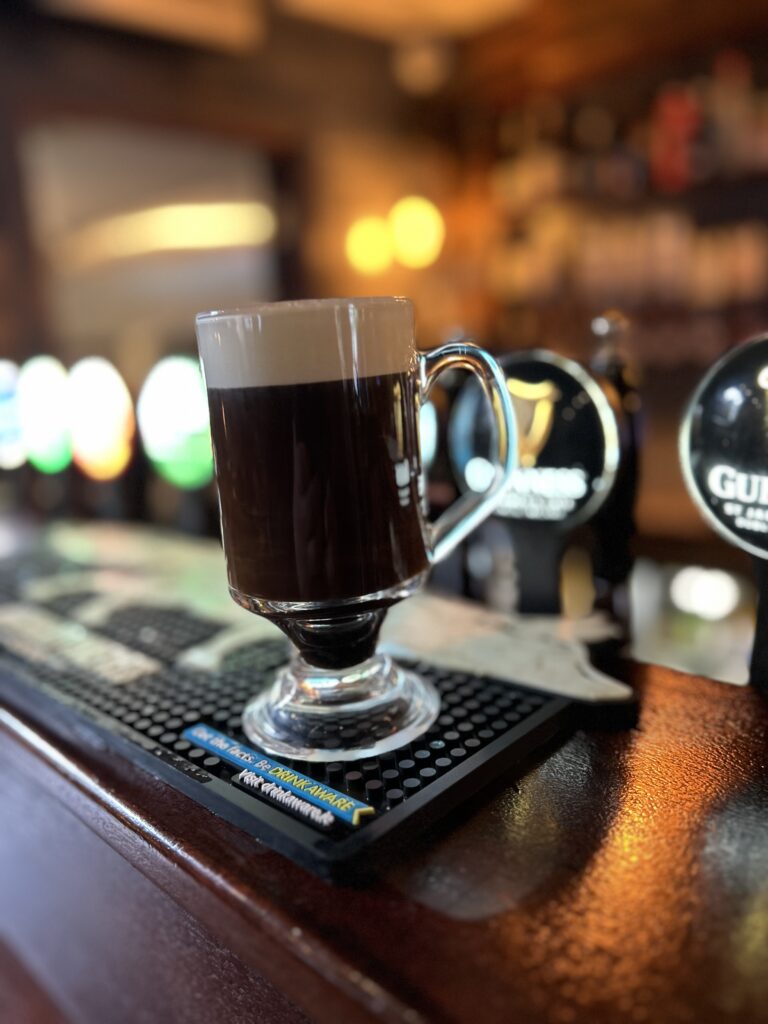 Irish Coffee in Sean's Bar. Im Hintergrund sind die historischen Zapfsäulen und ihre Medaillons unscharf zu erkennen.