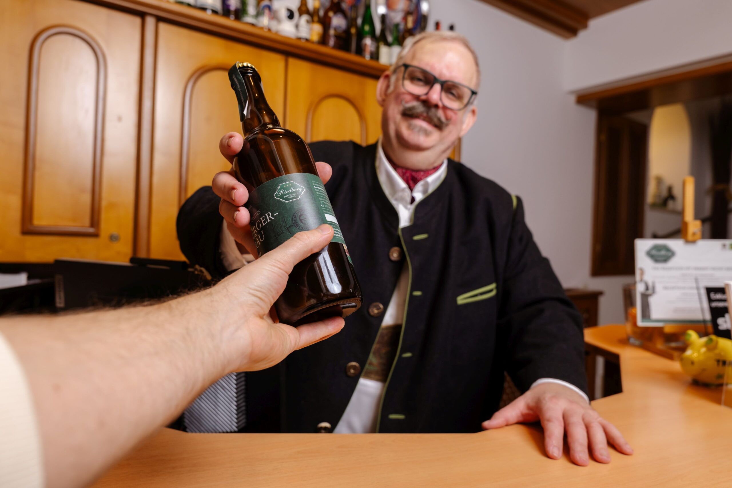 Ein Gast erhält an der Rezeption des Biergasthof Riedberg eine Flasche Bier zum Mitnehmen von Wirt und Hotelier Karl Zuser jun. überreicht