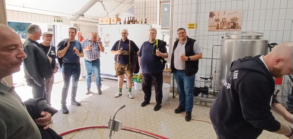 Teilnehmer mit Verkostungsgläsern zwischen Brauanlage und Edelstahltank beim Bierwochenende „Von Sudkessel zu Sudkessel“.
