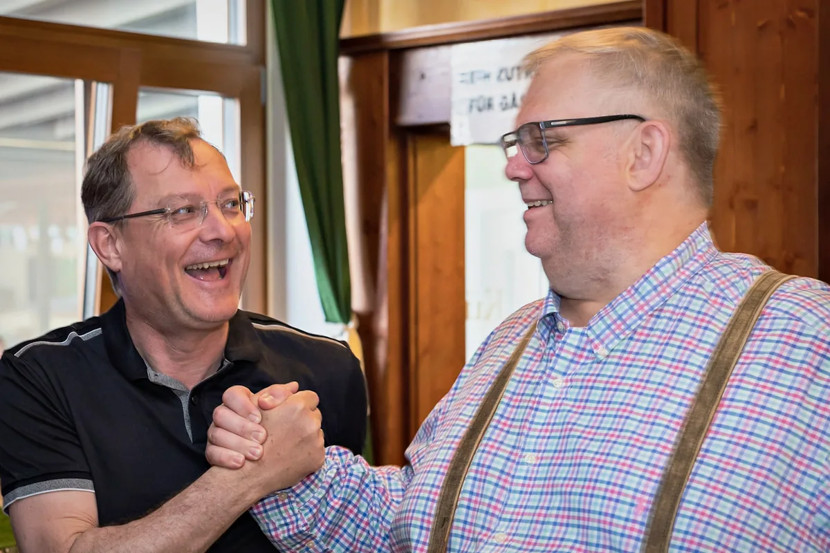 Zwei Männer lachen beim kräftigen Handschlag im Wirtshaus