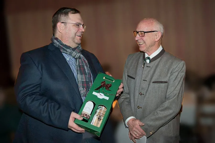 Zwei Herren lachen bei der Übergabe eines Biergeschenks im Wirtshaus