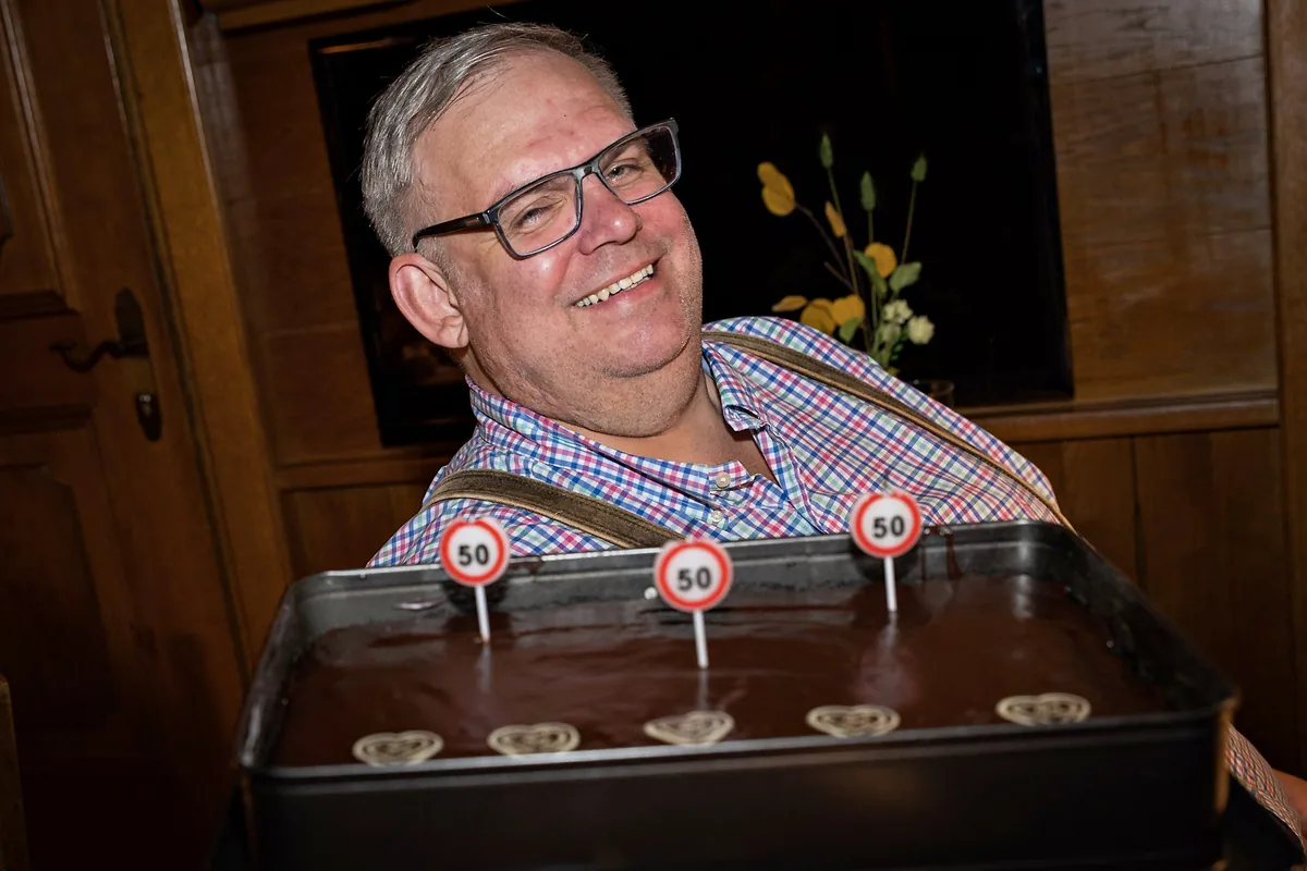 Strahlender Mann mit Geburtstagstorte und Zahlenkerzen zum runden Geburtstag