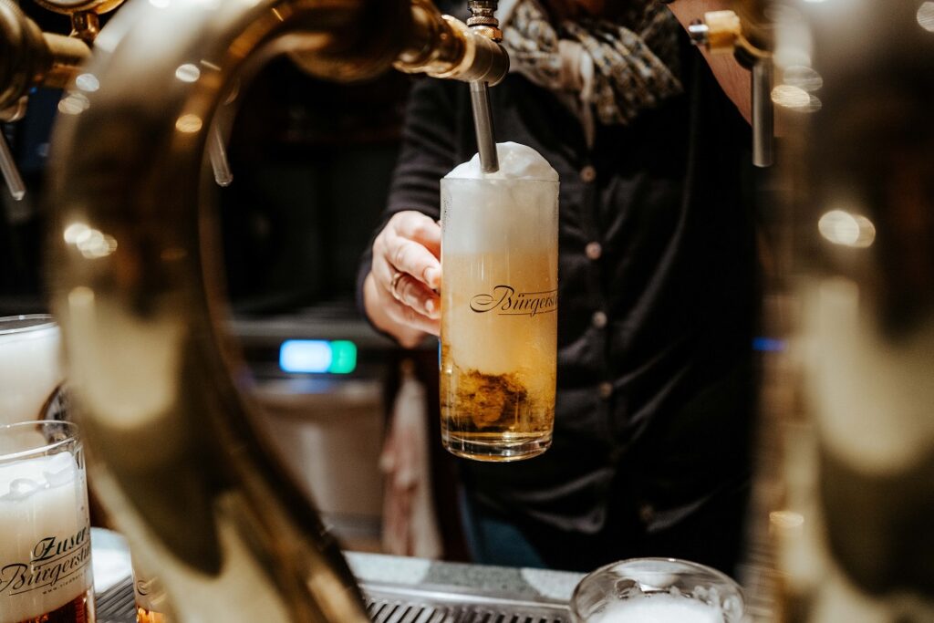 Österreichisches Märzen wird am Riedberg in einen gläsernen Bierkrug gezapft, im Bier wirbelt der Schaum auf.