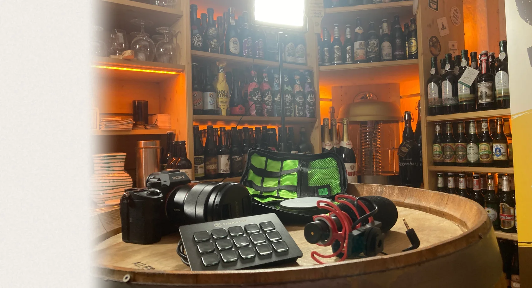 Technik-Set für Film, Radio und Podcast auf einem Bierfass im Bierkeller des Biergasthof Riedberg: Kamera, Mikrofon, Steuerpult und Videoleuchte vor beleuchteten Bierregalen